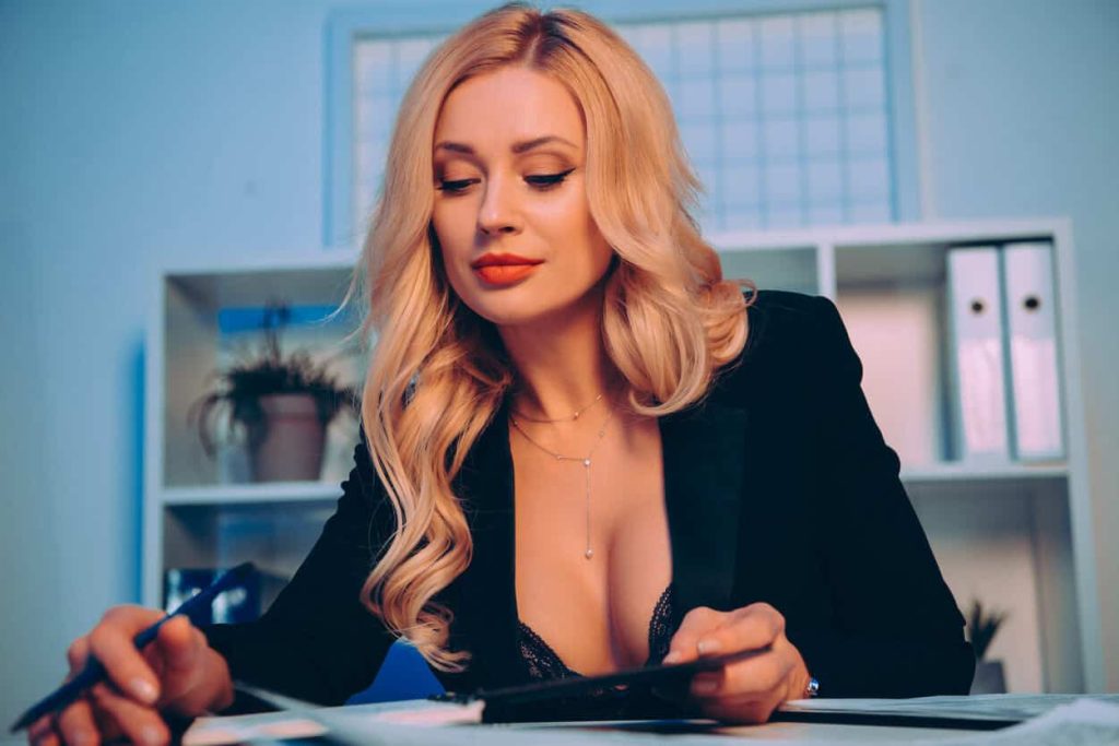 a blonde milf wearing a black sexy dress is showing her cleavage while writing on paper