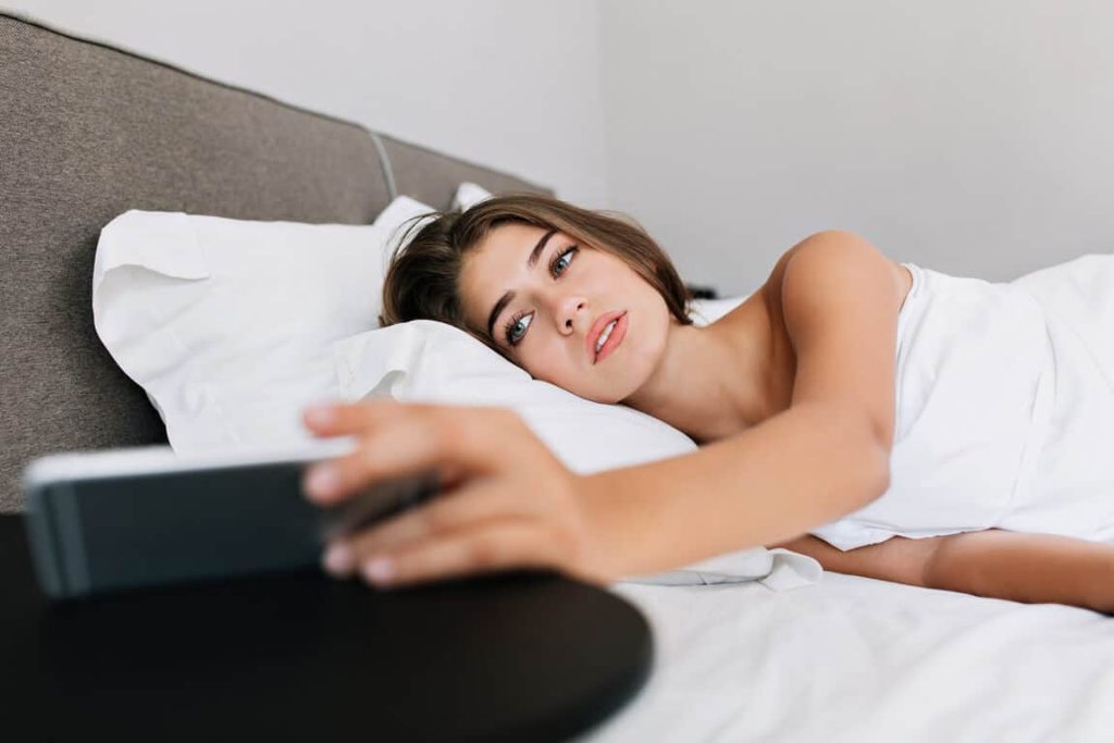 a naked woman who is holding her phone is sexting on whatsapp on her bed