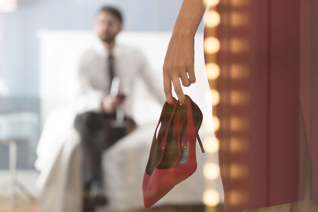 a naked escort woman from san antonio is holding her red stiletto while a man waits for her at the bed