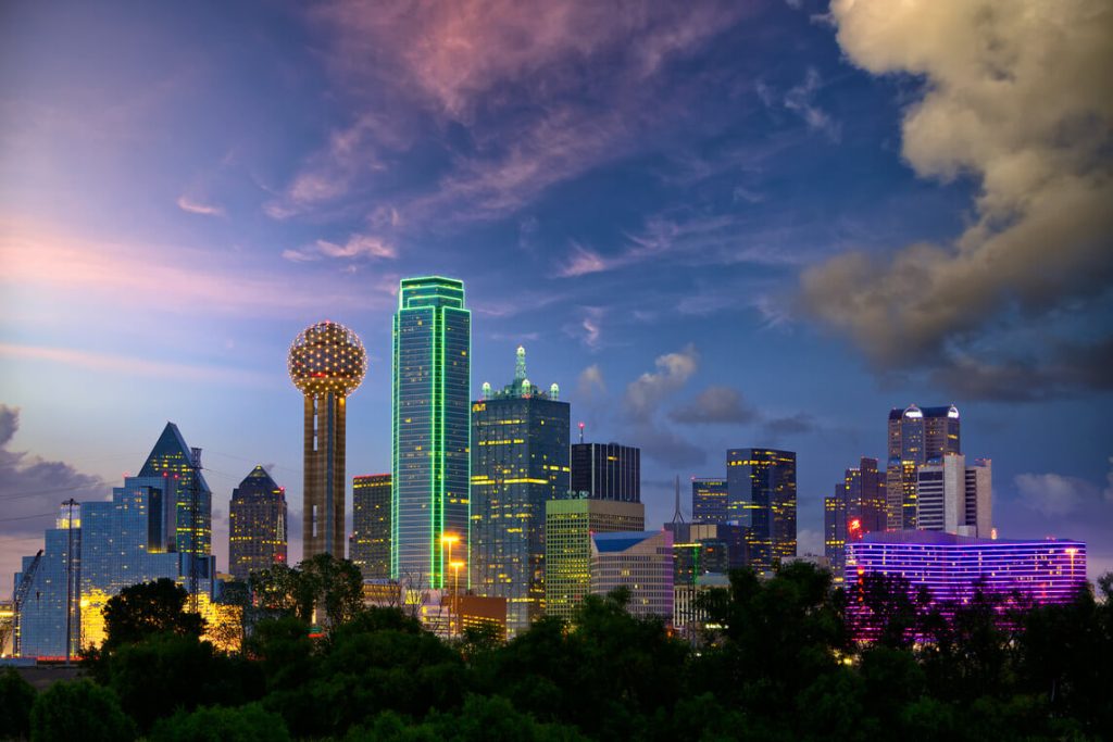 a picture of dallas at dusk with buildings full of lights at the background