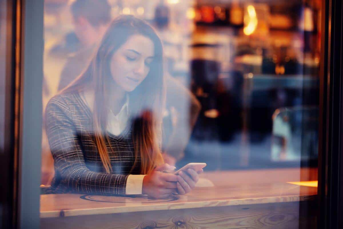 a single woman holding her phone on a bar while waiting for her order